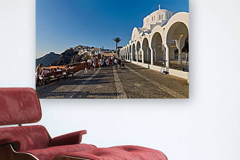 Crowds walk past white church cliffside town in Santorini. by Marco Brivio