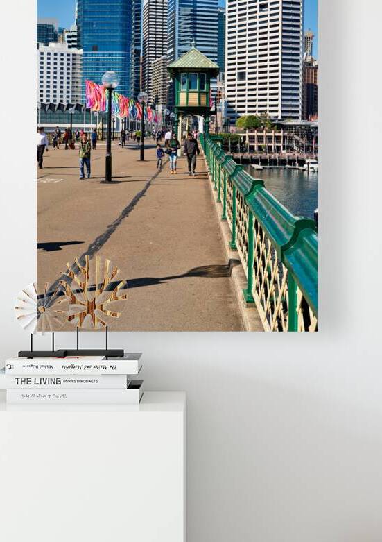 People walk along a waterfront promenade with city skyline. by Marco Brivio