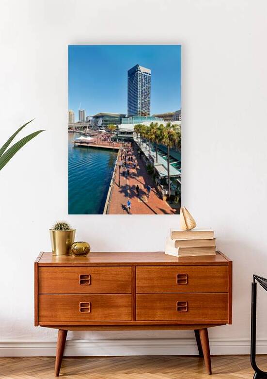 People walk along a sunny waterfront promenade with palm trees. by Marco Brivio