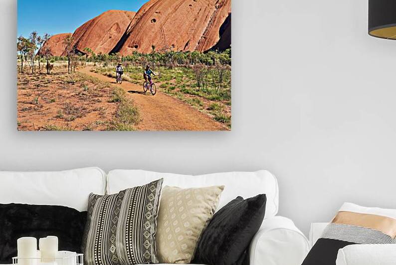 Two cyclists ride on a dirt path near Uluru Australia. by Marco Brivio
