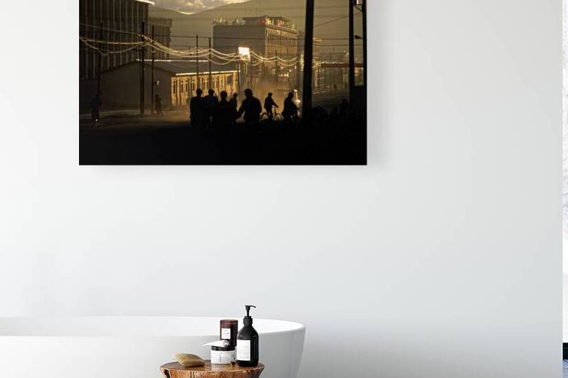 People walk and ride bikes along a dusty street at sunset in Tib by Marco Brivio