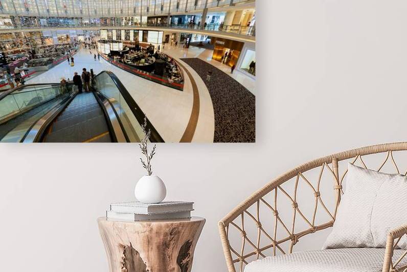 Busy shopping mall in Dubai with escalators and various stores by Marco Brivio