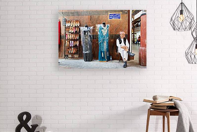 Man sits by shoes and dresses while relaxing in Dubai market by Marco Brivio