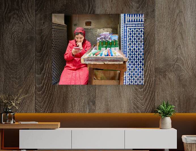 Woman using smartphone in Fez Medina while sitting by a stall by Marco Brivio