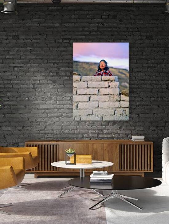 Young girl smiles over stone wall at sunset. by Marco Brivio