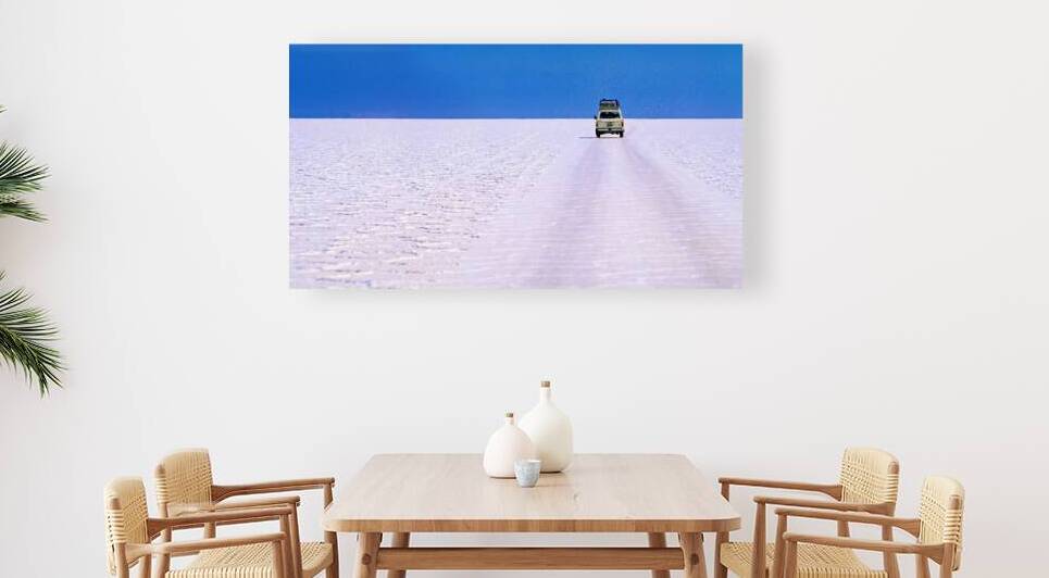 Van driving across vast white salt flat under blue sky. by Marco Brivio