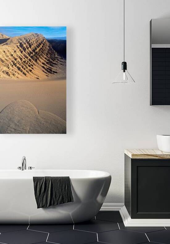 Eroded desert mountains and rippled sand under blue sky. by Marco Brivio