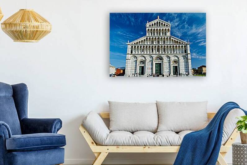 Visitors walk around Pisa Cathedral in Piazza dei Miracoli. The tall structure stands under a blue sky. People enjoy the lively atmosphere. by Marco Brivio